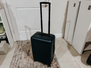 Black hardshell suitcase on the floor in front of a white door with handle extended