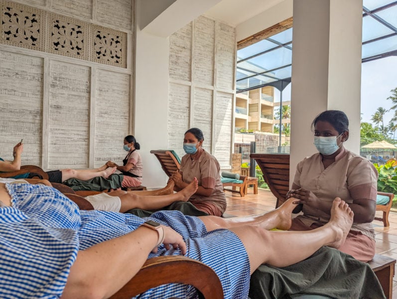 lower half of a girl in a blue dress lying down recieving a foor massage from a lady wearing a beige top and a face mask