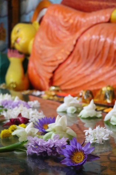 flowers in front of a stature of buddha lying down in an orange robe