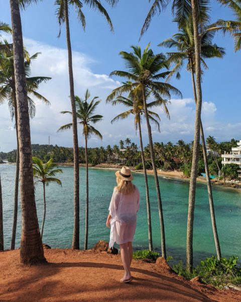 Emily wearing straw hat and white kaftan on a hill surrounded by palm trees with the see below, visiting Mirissa on a 2 weeks sri lanka itinerary  