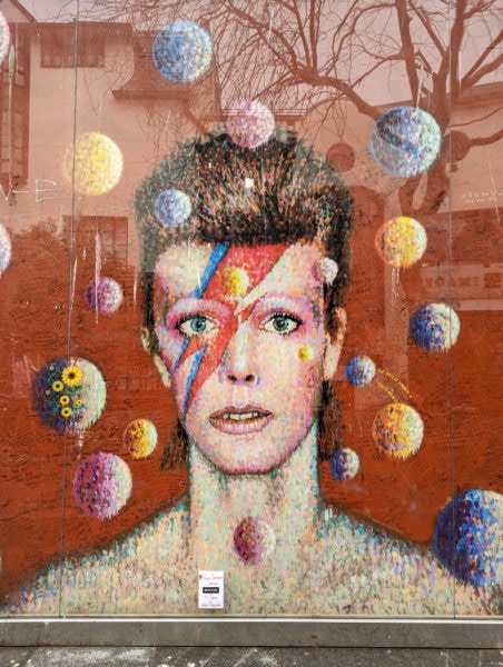 red wall with a mural of david bowie as ziggy stardust with red and blue lightning stripe across face
