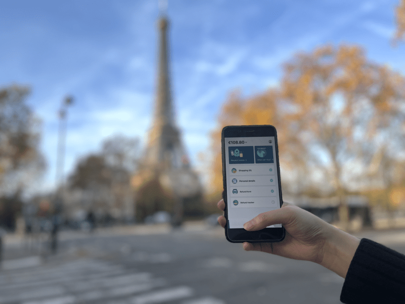 Phone showing the Wevat app for claiming vat back when shopping in france, held out by a hand in front of the eiffel tower
