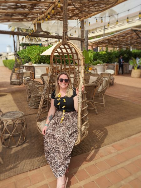 Emily wearing a black t shirt and leopard print skirt and sitting in a wooden swing chair at a beach bar in Colombo Sri Lanka