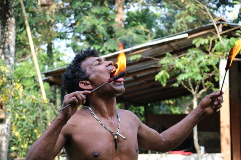a topless man putting fire on the end of a stick into his mouth in Kandy, Sri Lanka 