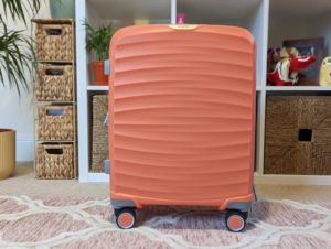 Small peach coloured hard suitcase on the floor infront of a shelving unit