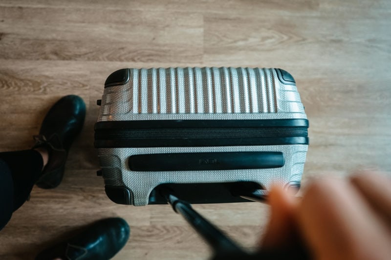 lookinng down at a woman's feet next to a carry on luggage case with her hand holding the handle