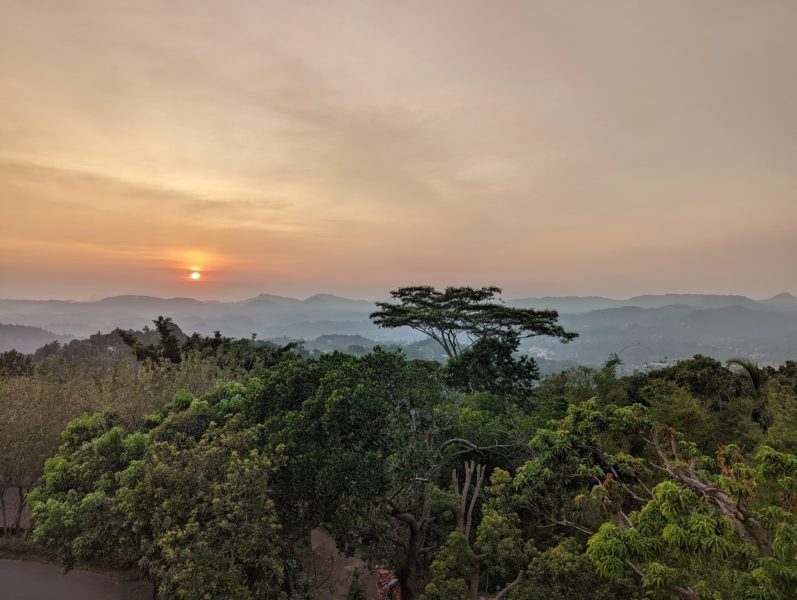 looking across tropical green forest at a setting sun in a hazy orange sky in Kandy Sri Lanka