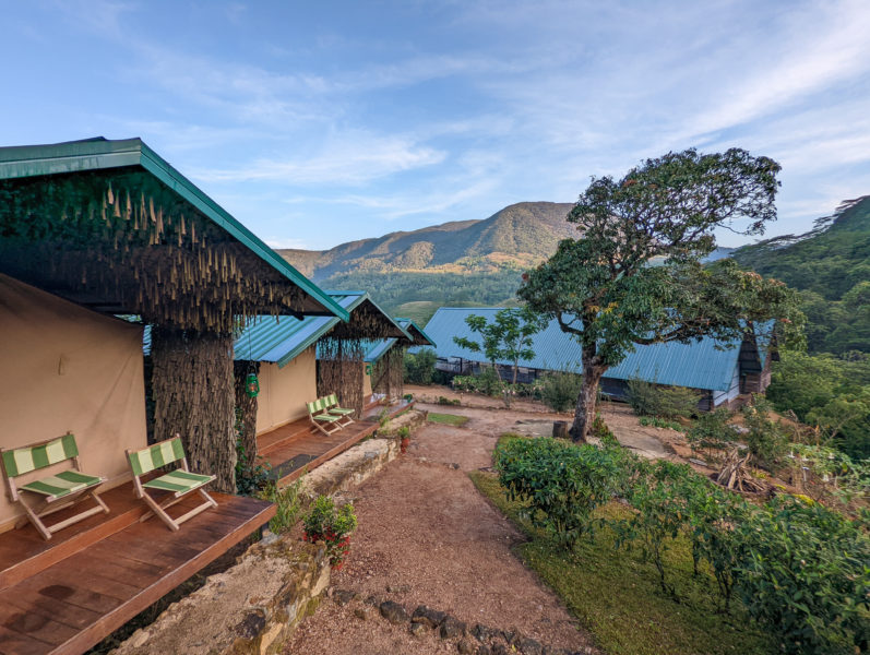 safari tent with two deckchairs outside. A path runs next to it towards a low building with a blue tin roof and a mountain behind that. Glamping adventures in Sri Lanka. 