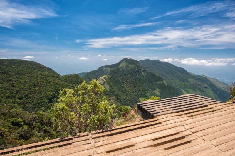 wooden viewing platform overlooking a valley and green forested mountains beneath a blue sky