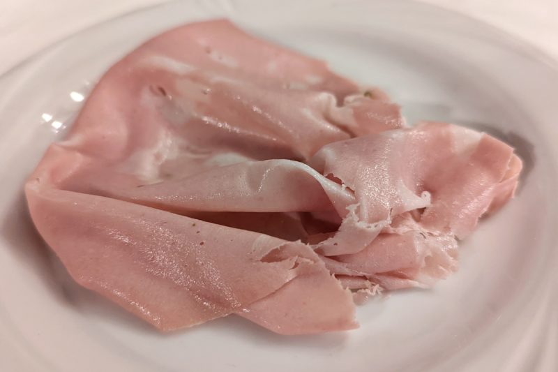 close up of a slice of pale pink ham on a white plate