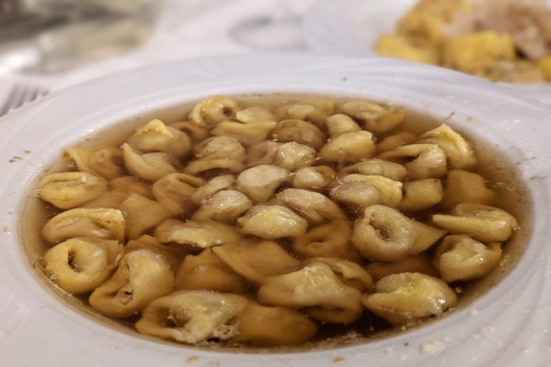 close up of a white bowl filled with thin brown broth and stuffed pasta shapes