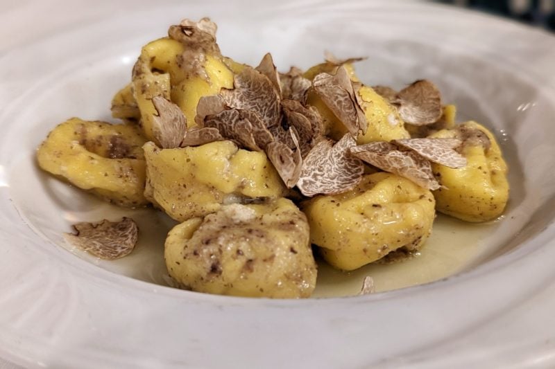 close up of a white plate with large filled pastas and pieces of light brown truffle shavings
