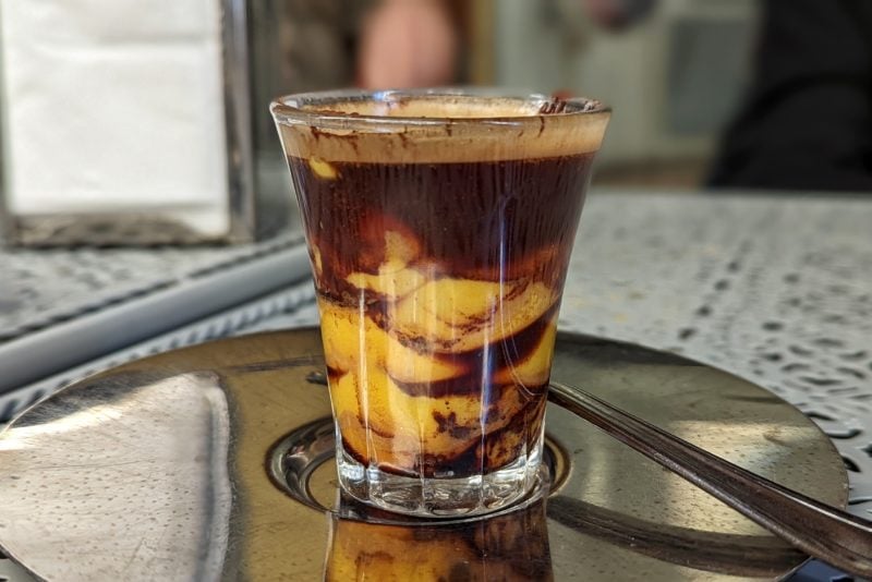 close up of a shot glass containing a swirled mix of yellow custrd with dark brown espresso at a coffee shop in bologna italy