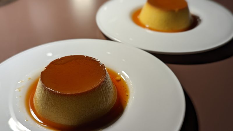 close up of two white plates with a circular dessert that looks like a cream coloured pannacotta topped with a golden brown caramel sauce
