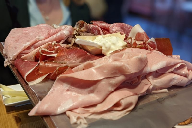 close up of a grey rectangular platter loaded with multiple pieces of ham and a small pot of soft white cheese