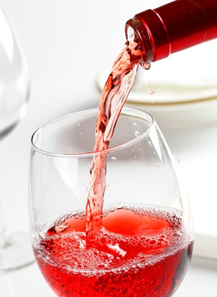 close up of a bright red wine being poured into a wine glass on a white tablecloth