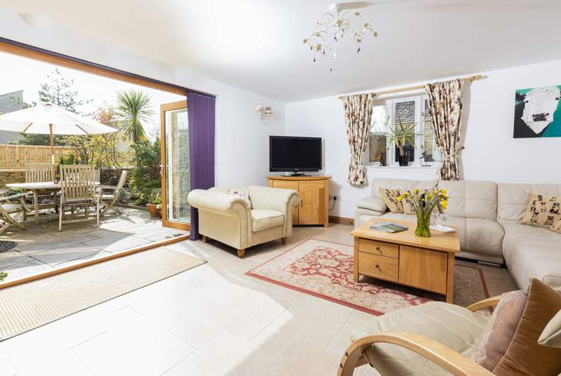 a lounge with white walls and floors and a cream leather sofa with large patio doors open and a patio outside on a sunny day