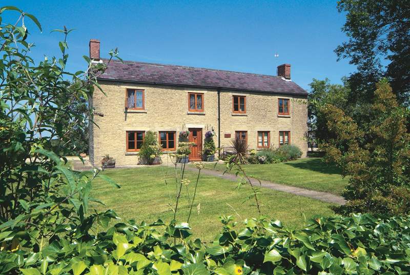 cottage built from beige stone and a grey roof with a fgreen lawn in front