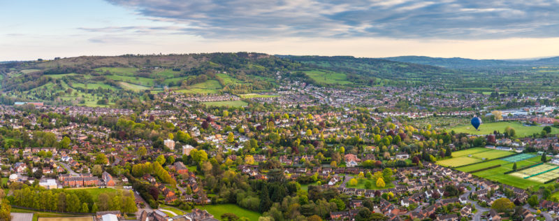 Dramatic aerial view of idyllic rolling patchwork farmland and houses with pretty wooded boundaries, lit in warm early evening sunshine in the heart of the Cotswolds, England - Weekend Itinerary for Gloucester and Cheltenham