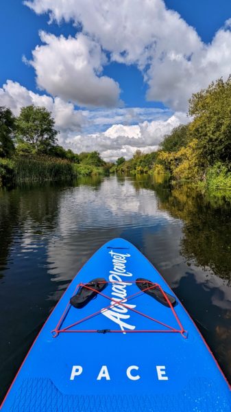 nose of a bright blue paddleboard on a river with trees and blue sky in the background