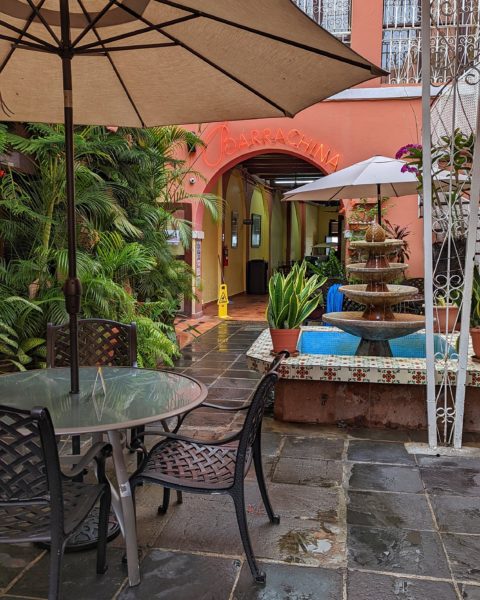 courtyard of a bar in san juan pr with a glass table with an umbrella and a fountain in the background