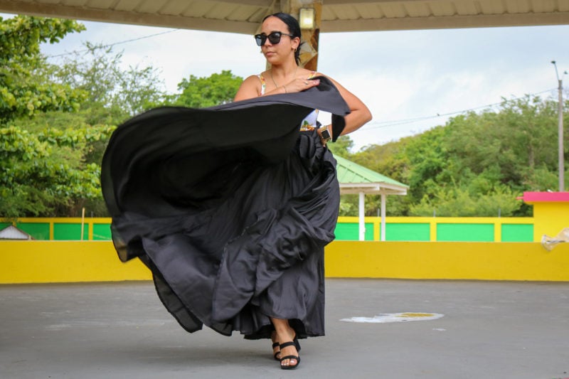 bomba dancer wearing a white flowery top and sunglasses and a long black skirt which she is holding out while she dances to make the fabric flow - unique things to do in puerto rico