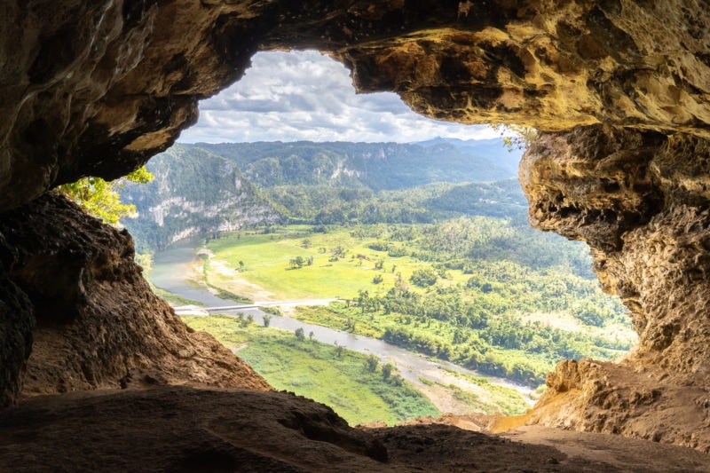 a natural window formed by the opening of a cave looking down towards a green landscape and a river far below - fun things to do in puerto rico