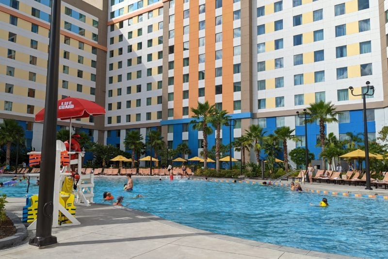 a hotel with an orange and yellow patterned facade standing behind a bright blue pool. budget accommodation at universal studios in orlando florida