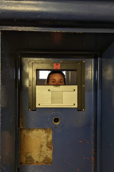 emily looking out of an opening in a blue painted cell door in gloucester prison. you can only see the top half of her face. 