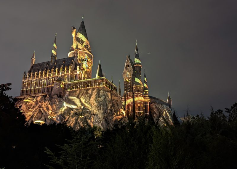 Hogwarts Castle at night lit up with gold patterned progections and the shape of the Hogwarts crest -  how to do universal studios orlando on a budget
