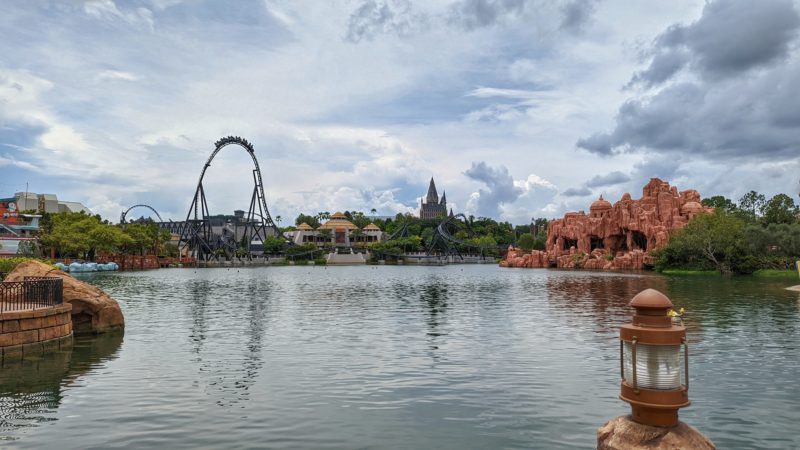 View of Universal Islands of Adventure across a lake on a cloudy day with a train going over the top of a tall section of rollercoaster track 