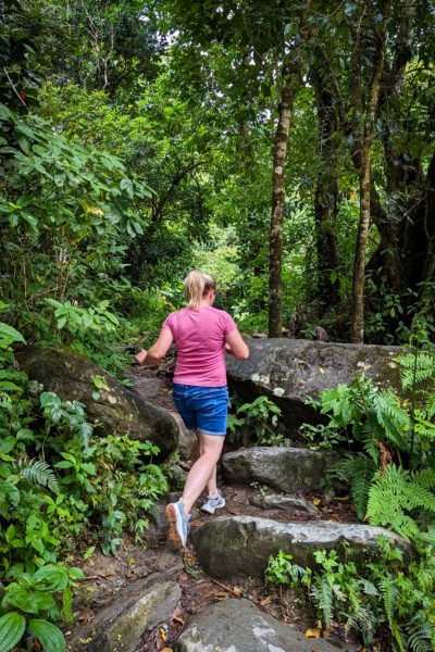 Emily wearing denim shorts and a pink sports t shirt with her hair in a ponytail running up some stone steps in a rainforest with dense green trees in the background - unique things to do in puerto rico