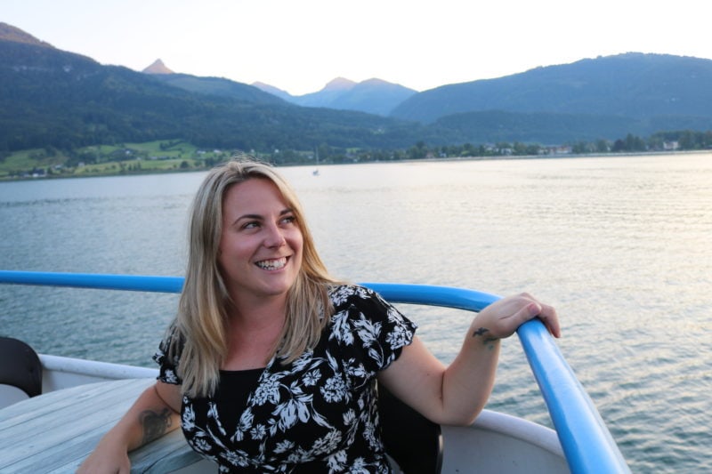 emily sitting on a boat at sunset wearing a black dress with white flowers with a lake and mountains behind. Summer city break packing list. 