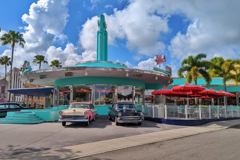 a bright turquoise circular building wiht a pink sign saying Mel's Diner and two retro American cars in front of it - based on the set of American Graffiti - one of the cheap places to eat at Universal Studios Orlando