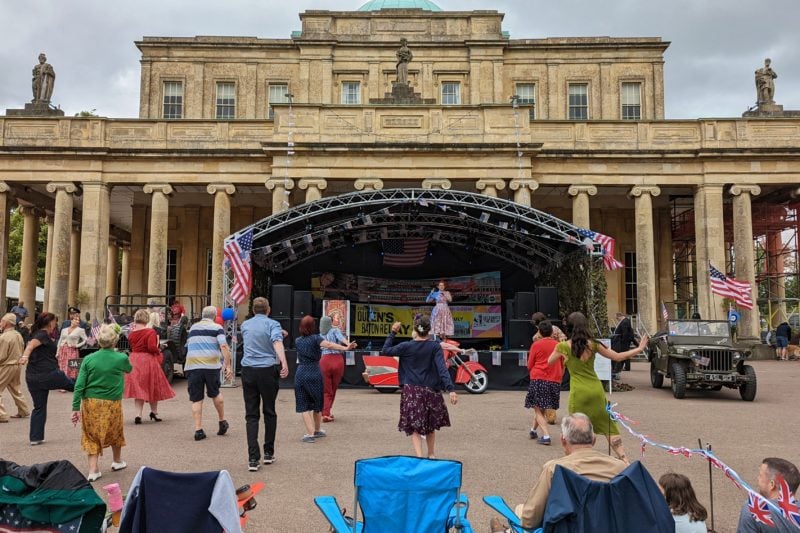 people dnacing in front of an outdoor stage in front of a large classical building with lots of columns