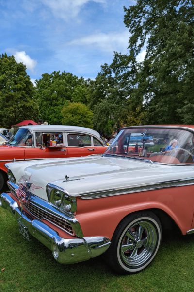 a pink and white classic american car with the us flag on the bonnet