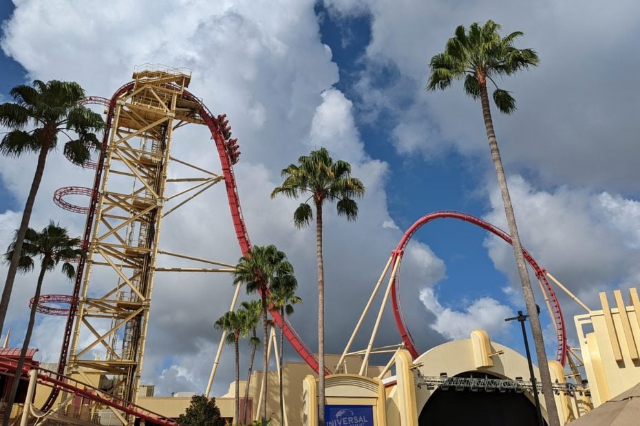 top of a red rollercoaster and tall palm trees against a blue sky with fluffy clouds - how to do universal studios orlando on a budget