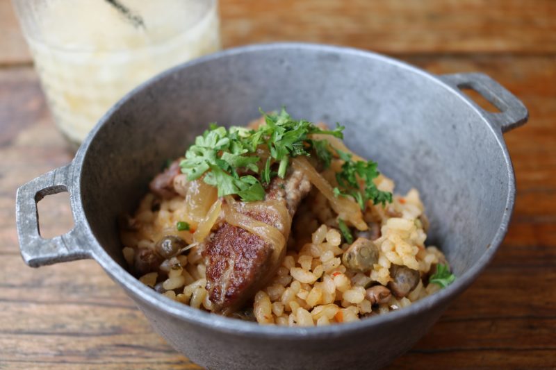 small grey bowl filled with rice and meat on a wooden table with a cocktail in the background