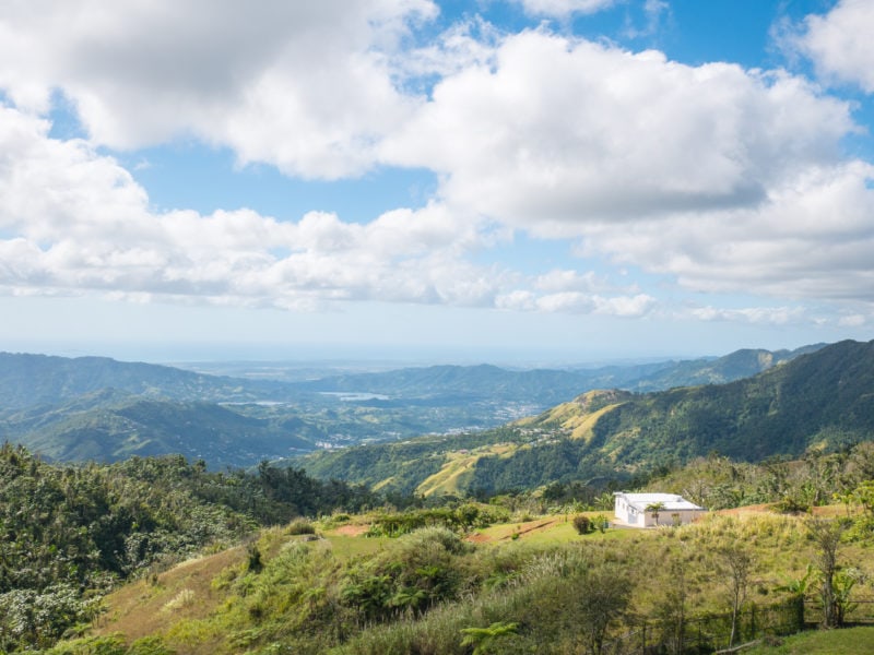 view of a green mountain landscape on a sunny day with a blue sky filled with fluffy white clouds