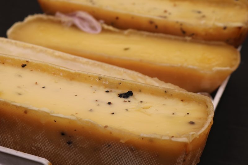 close up of three cheese wheels which have been cut in half. the closest one has small black pieces of truffle in it.