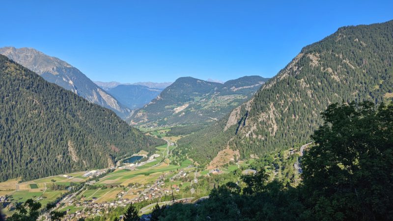 landscape of a lush green valley on a very sunny summer day with the town of verbier visible in front of the green forested mountains