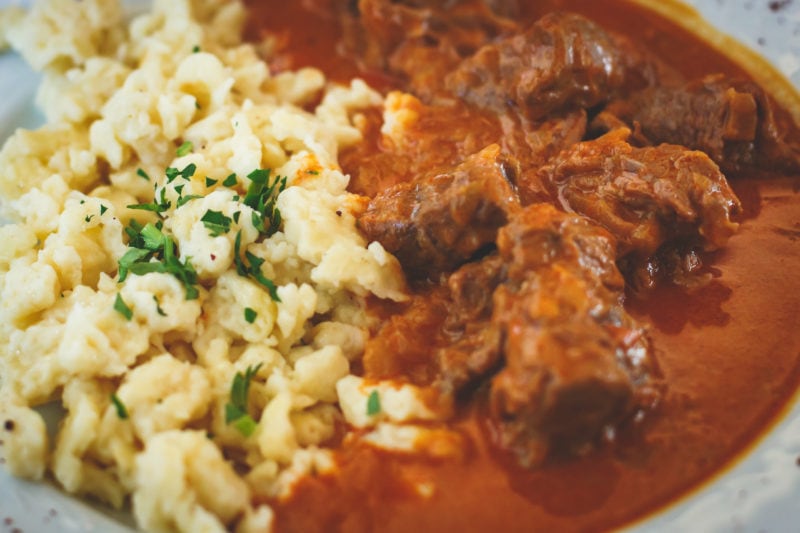 close up of a white plate with mashed potato on the left and a thick red sauce with lumps of beef on the right