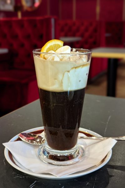 close up of a glass filled with black coffee and topped with whipped cream and a slice of orange