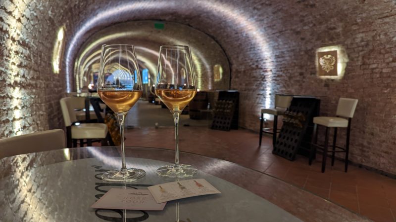 two wine glasses of rose champage on a table in a dimly lit stone cellar with arched cieling in vienna austria