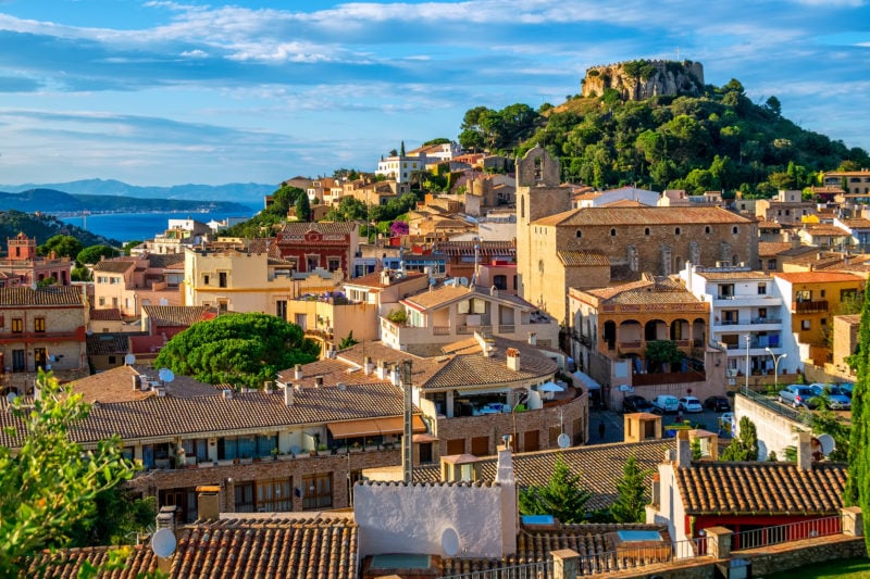 aerial viewpoint of a colourful spanish town with a castle on a green hilltop in the centre and the sea just visible behind. begur is one of the best places to visit in costa brava spain. 
