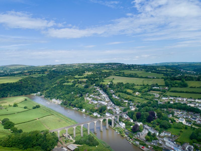 drone view of a large river with a stone viaduct across it in green countryside with many hills and lines of hedgerows