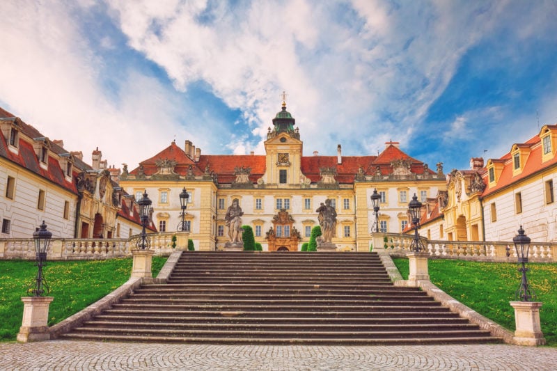 Old historic castle in Valtice, South Moravia. Yellow stone exterior with orange roof. there are stone steps leading up to the castle. sunny day with blue sky. 