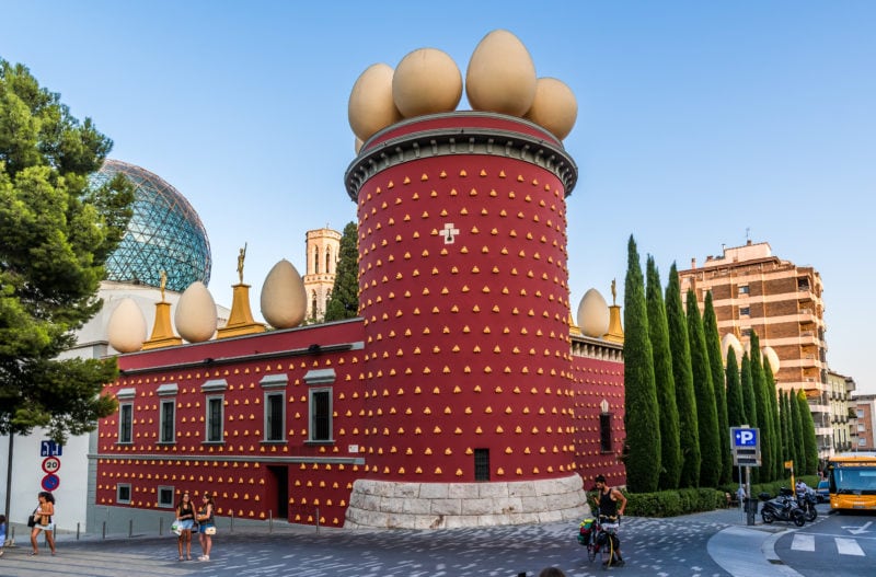 red castle wall with golden egg shaped decorations on top against a blue sky - the dali museum in figueres spain