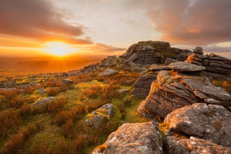 sunset behind a pile of granite boulders on a grassy hill in Dartmoor - one of the best places to visit in south devon