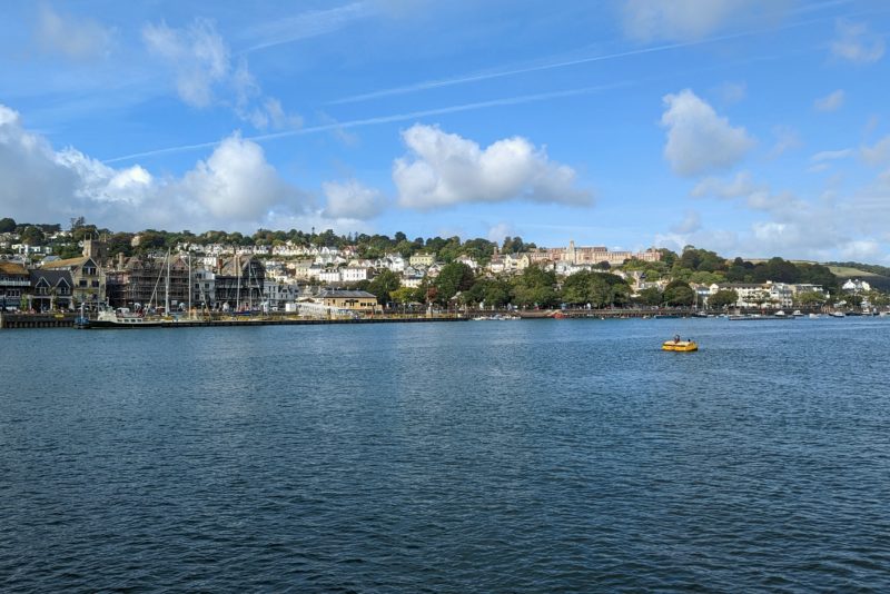 blue river with a town full of white houses on the far bank beneath a blue sky. dartmouth in devon.
